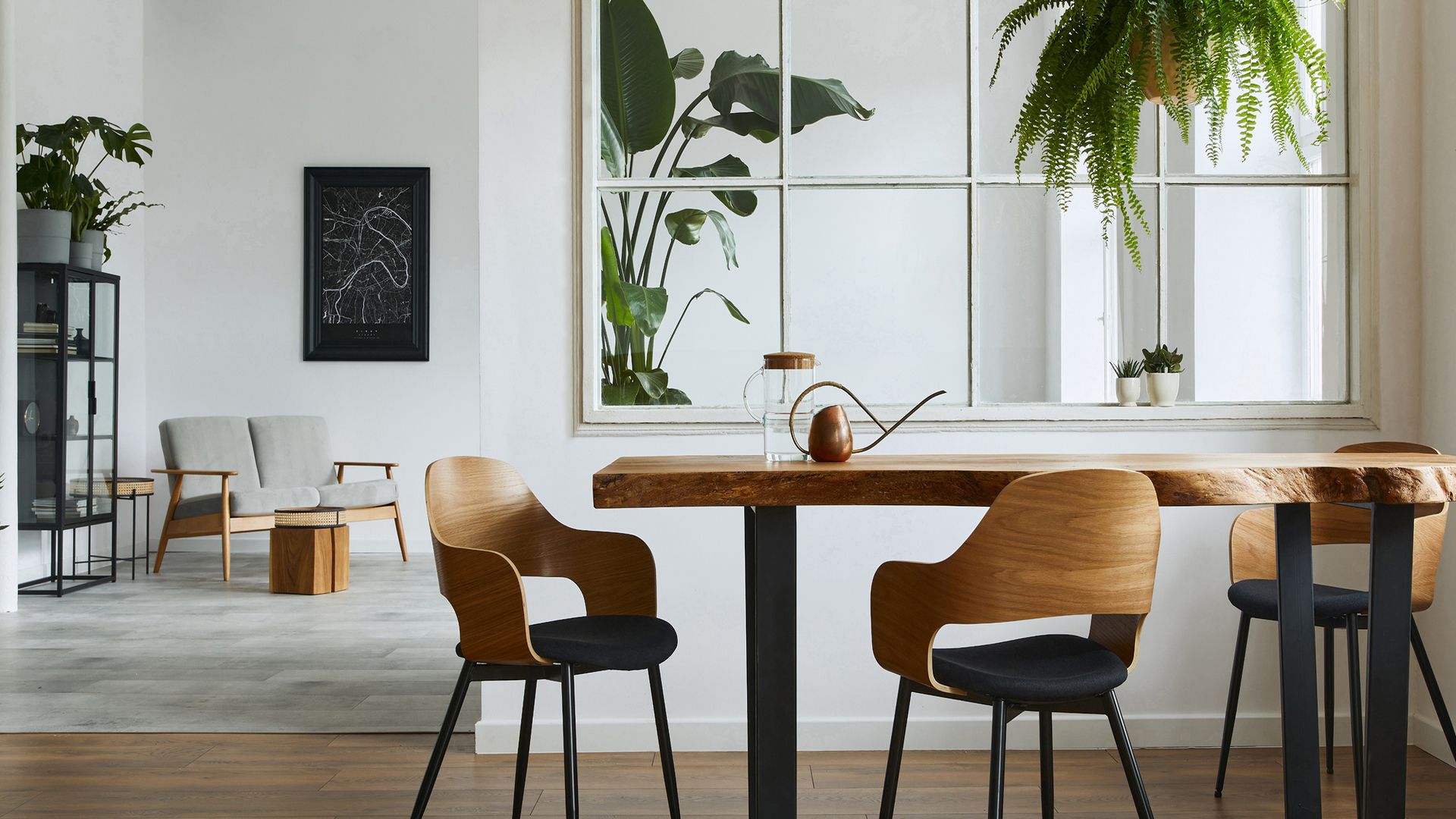Modernes, helles Esszimmer mit einem massiven Baumkante-Holztisch, stylischen Holzstühlen mit dunklen Polstern und zahlreichen grünen Zimmerpflanzen vor einem großen Fenster